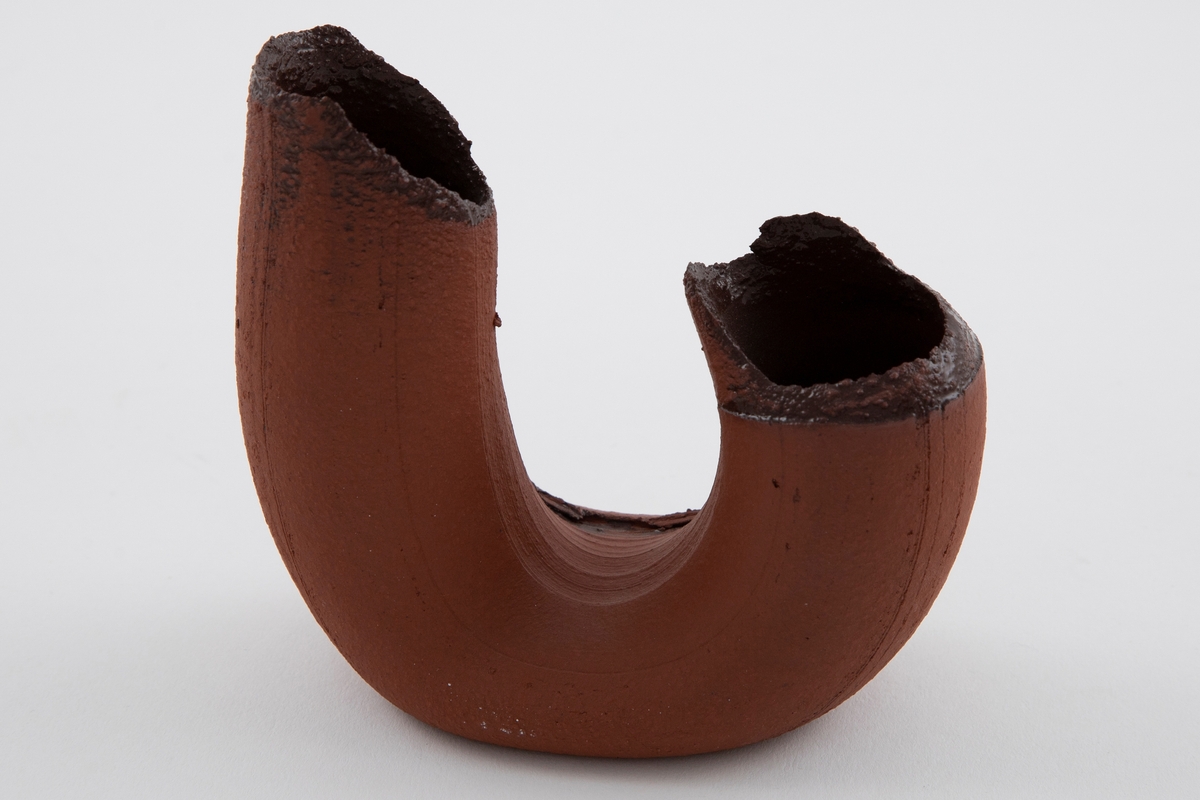 Vase i matt brun terrakotta. Asymmetrisk U-form med riller. Åpne munninger med ujevne render. Mørkebrunglasert på innsiden.