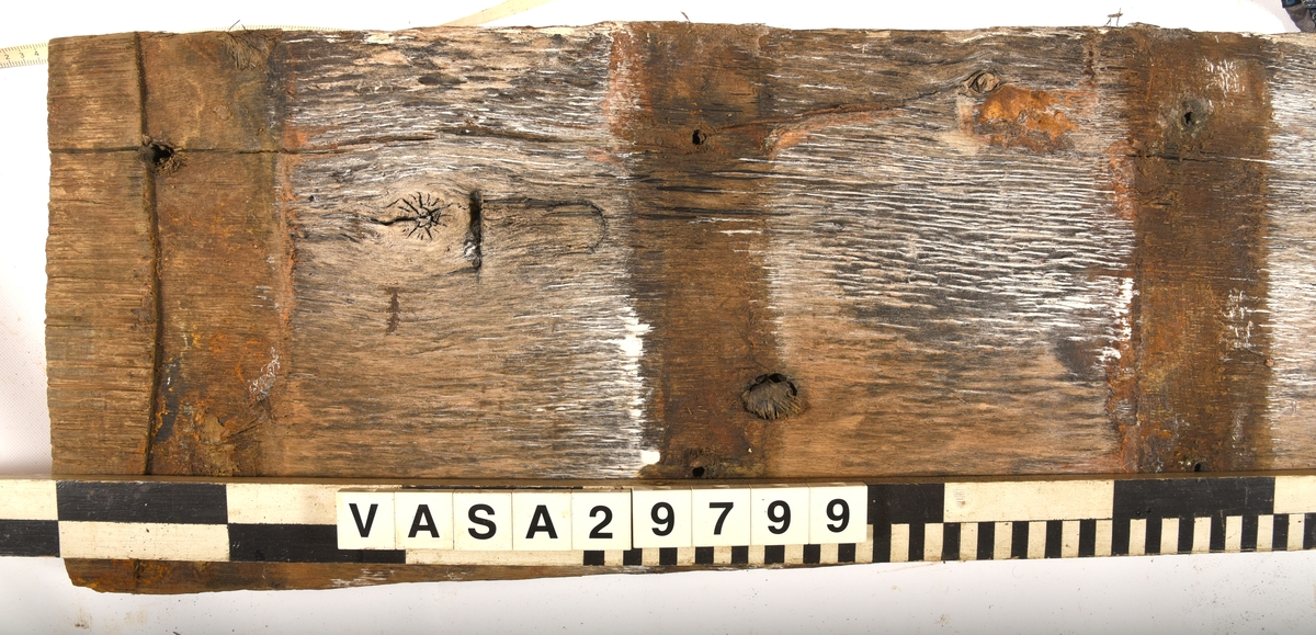 Däcksplanka i ek.
Totalt 15 genomgående spikhål, 8 längs plankans ena sida och 7 längs den andra.
En kvarsittande dymling
Undersidan är täckt av små sprickor samt har tydliga avtryck från ribbor och däcksbalkar.
Undersidan har också en ristning som liknar ett "J".