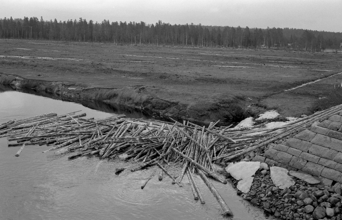 Tømmervase ved brukar. visstnok i elva Nordre Osa i Åmot, som renner inn i nordenden av Osensjøen. Dette bildet er fra 1961. Fotografen har stått på brua med kameraet vendt mot det nedenforliggende vannspeilet og tømmeret som hadde samlet seg i en haug der. Dette året ble det innmeldt 131 864 tømmerstokker til fløting i Nordre Osa. Dette utgjorde 7,3 prosent av det antall stokker som var innmeldt i det som i fløtingsstatistikken kalles Rena med bivassdrag (alle vassdrag som til slutt endte i den nedre delen av Rena-elva). Nordre Osa hadde 14 prosent av det tømmeret som ble levert ved vassdrag som endte i Osensjøen og elva Søndre Osa.
