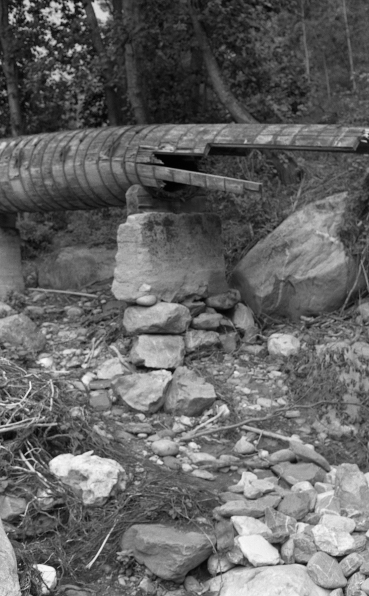 Brukket turbinrør nedenfor Tromsa Mølles dam i elva Tromsa på Fåvang i Ringebu kommune i Gudbrandsdalen. Fotografiet er tatt i 1958, etter at en brå og kraftig regnflom i pinsehelga dette året hadde gjort betydelige skader på dette anlegget og mange andre eiendommer ved den nedre delen av vassdraget. Den delen av turbinrøret som ses på dette  fotografiet var lagd av bord som var satt sammen til et sylindrisk rør og holdt ihop av forholdsvis tettsittende jerngjorder. Turbinrøret kvilte på betongpilarer med treforinger på toppen. Bildet viser hvordan røret hadde fått en bruddskade like ved en slik pilar. Vi aner også hvordan vannet som fosset ut av røret må ha vasket bort mye av jordsmonnet under rørgata, og at den støpte pilaren sto ustøtt på sammenrøyset stein uten bindemiddel.

Litt informasjon om flommen og den opfølgende skadetaksten finnes under fanen «Opplysninger».