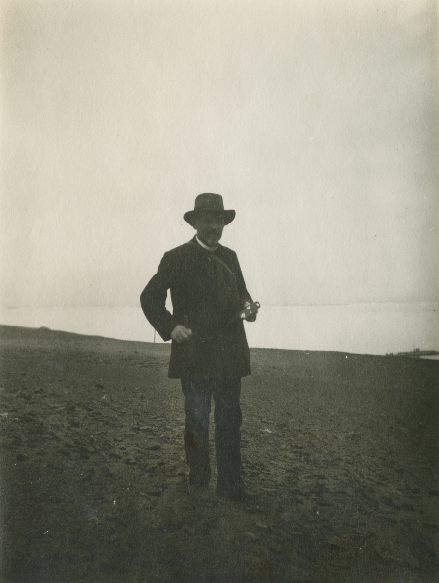 Fotografi från expedition till Peru 1920. Motiv av hattprydd Otto Nordenskjöld som står på en stenig strand.