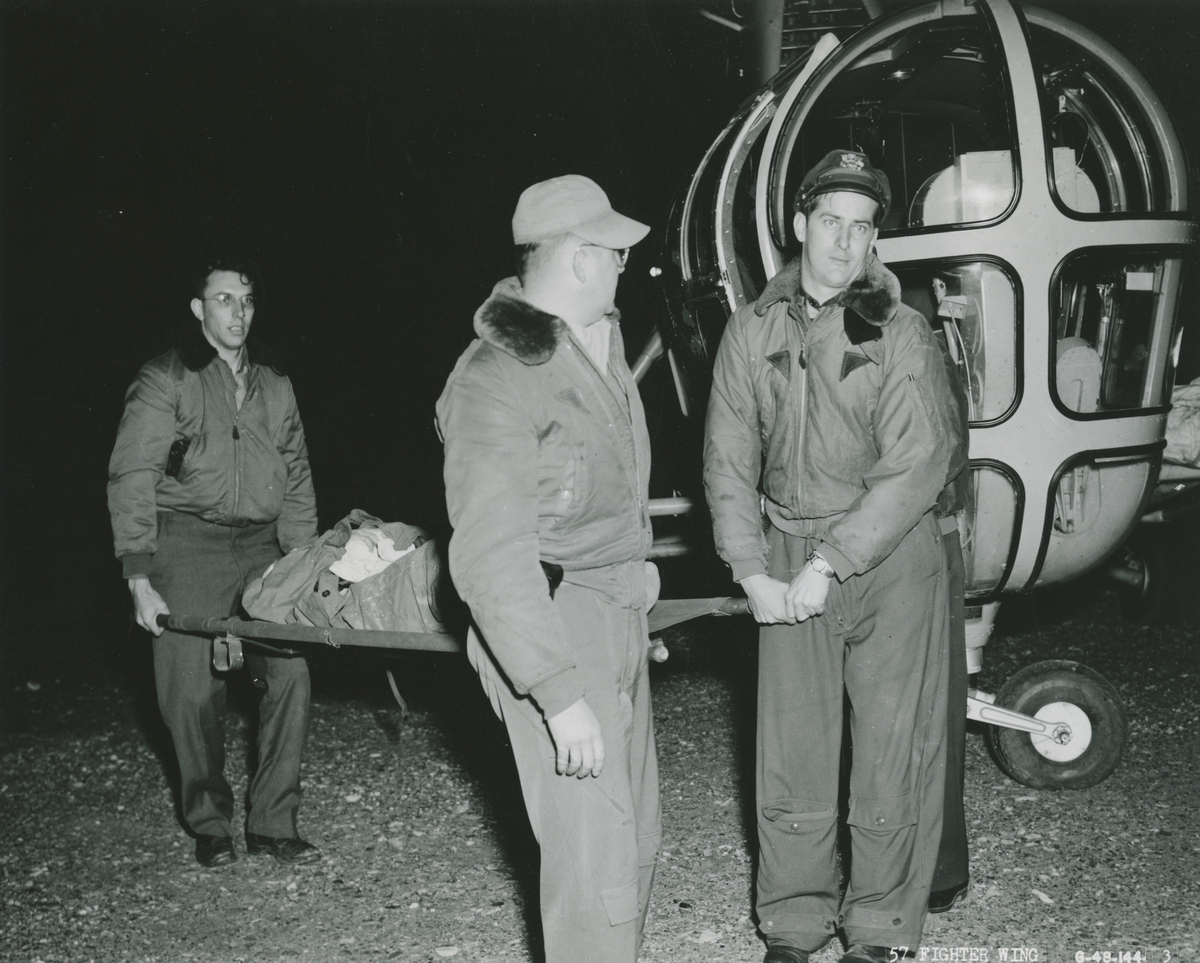 Fotografi från låda märkt Bernt Balchen. Balchen var norsk-amerikansk flygare, polarforskare och militär. Motiv av räddningsarbetare som bär en skadad man på bår vid en Skikorskyhelikopter.