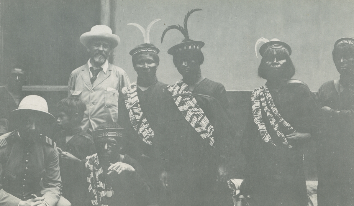 Fotografi från Peruexpedition 1920. Motiv av Otto Nordenskjöld tillsammans med flera män med fjädrar i håret och huvudbonader och vad som ser ut att vara högtidskläder. Nordenskjöld är mannen med skägg och hatt som står upp till vänster.