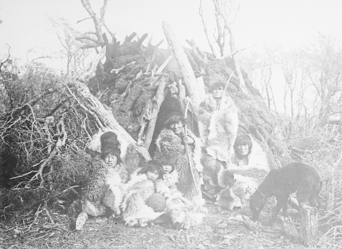 Fotografi från Eldslandet. Motiv av familj i djungel framför hydda.