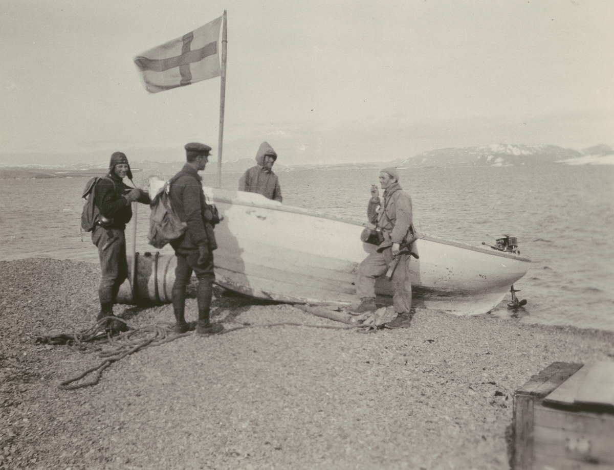 Fotografi från Ahlmannexpeditionen 1931. Motiv av fyra män vid båt på strand.