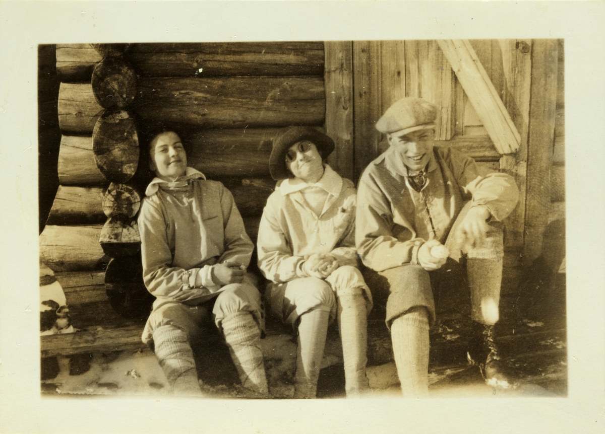 Lucy og Mimi Egeberg samt Johan Heuch Bugge hviler ved tømmerbu på vei til eller fra fjelltoppen Ruten ved Fefor. Fotografert påsken 1926.