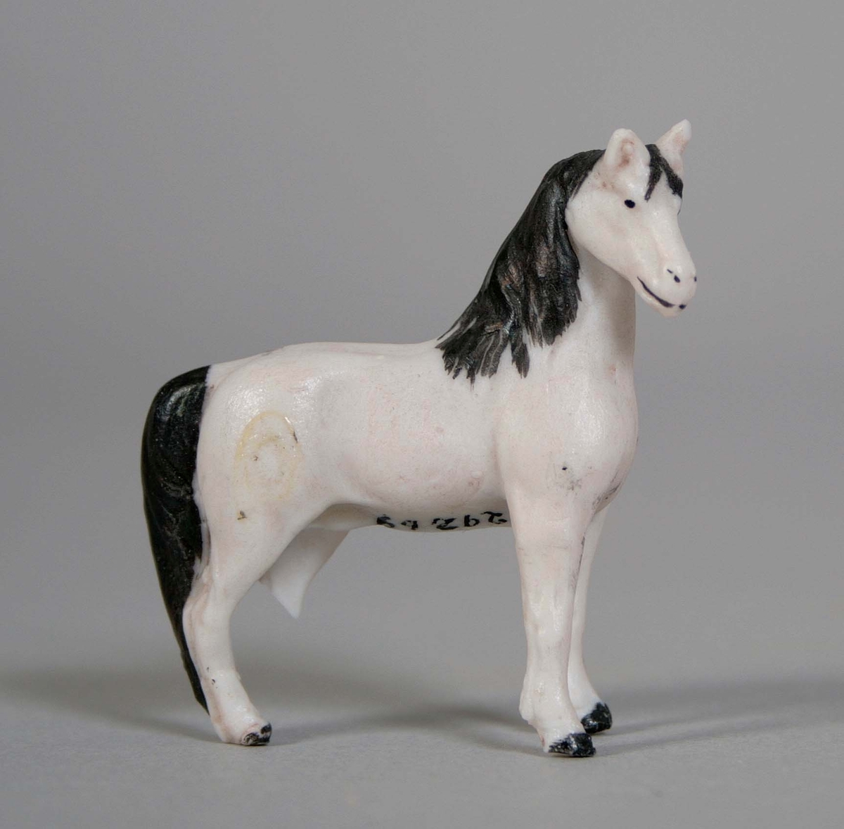 Stående häst, i oglaserat vitt porslin med svartmålad man, svans och klövar. Vänster bakben avbrutet (saknas).
