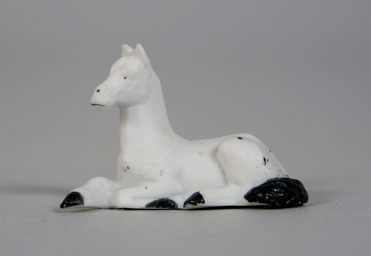 Liggande häst, i oglaserat vitt porslin med svartmålad svans och klövar.