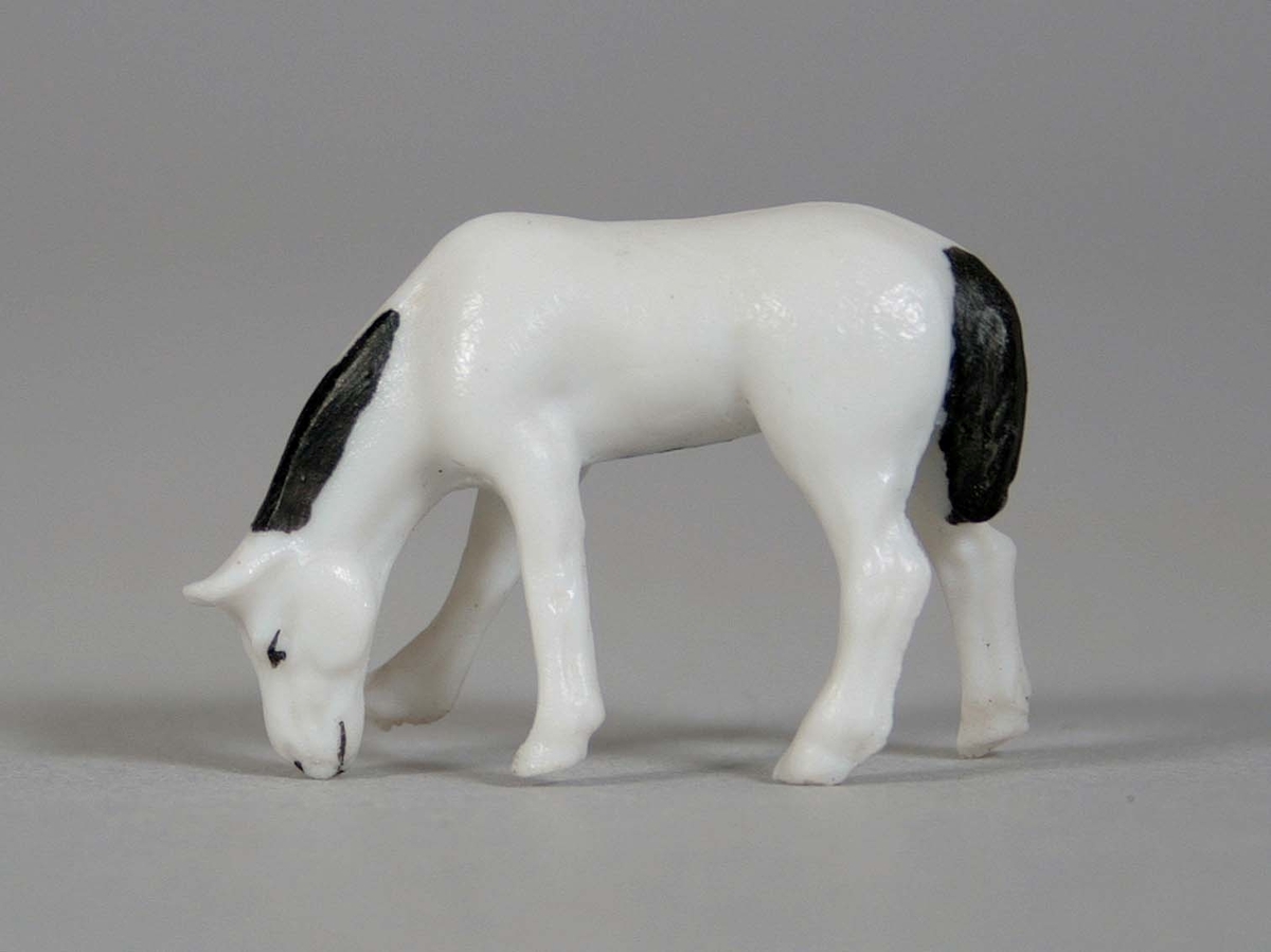 Stående, betande häst, i oglaserat vitt porslin med svartmålad man och svans.