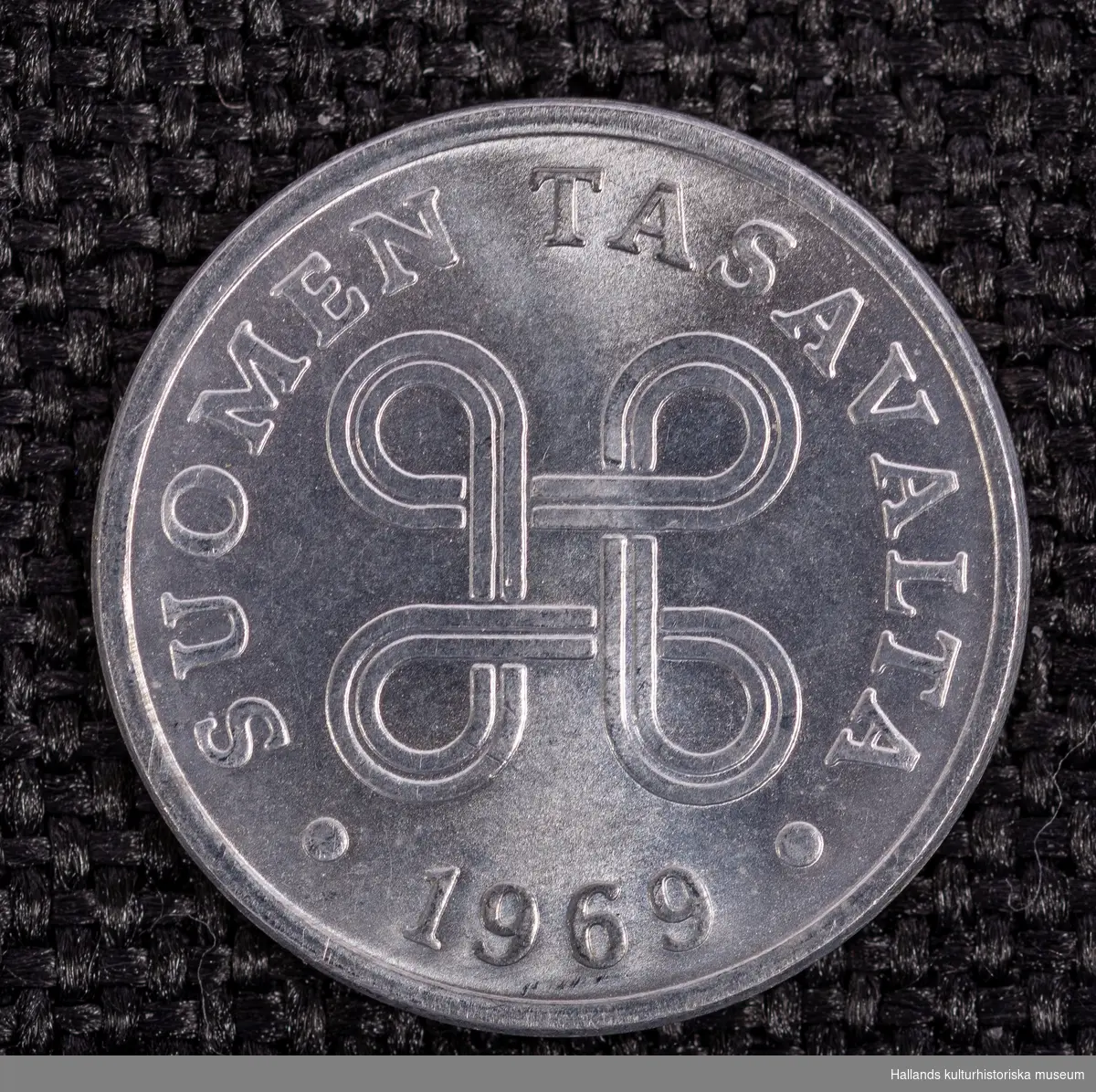 Två finska mynt av vitmetall (delar 1 och 2). Präglingsår 1969 respektive 1970. 1 penni.Diameter 10 mm. Åtsida: Präglingsår, dubbel swastika samt texten "SUOMEN TASAVALTA" (Republiken Finland). Frånsida: Valör. 