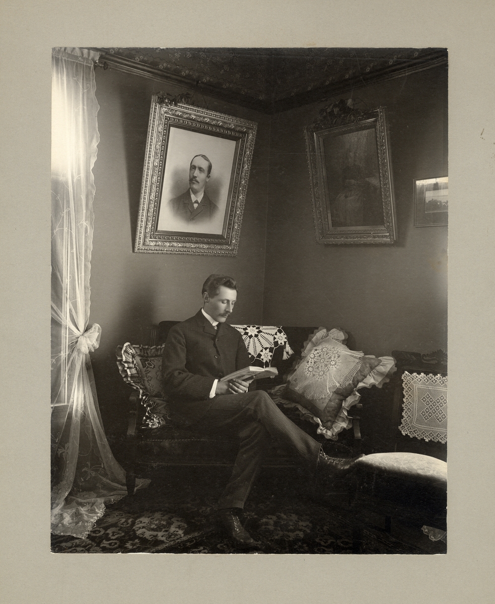 En okänd man i kostym sitter och läser i ett vardagsrum.