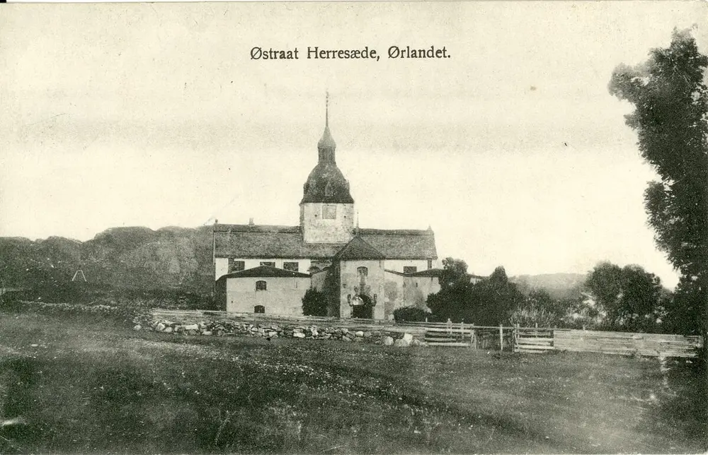 Svart-hvitt foto av Austråttborgen med landskapet rundt. Kvaliteten er kornete. Øverst står det med svart skrift "Østraat Herresæde, Ørlandet". Et gjerde i stein og planker omringer borgen.