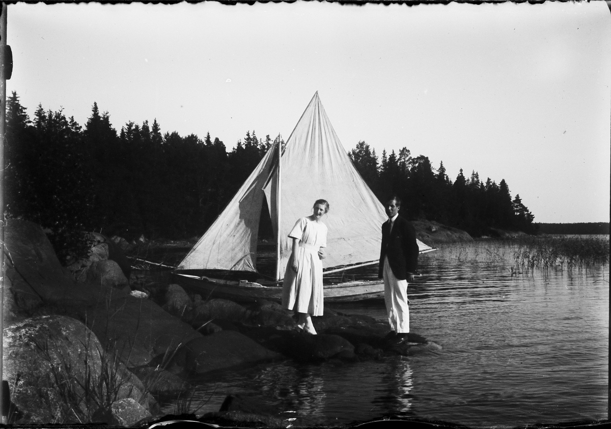 Sara Edhlund och man står på klipporna vid en liten segelbåt, Östhammar, Uppland
