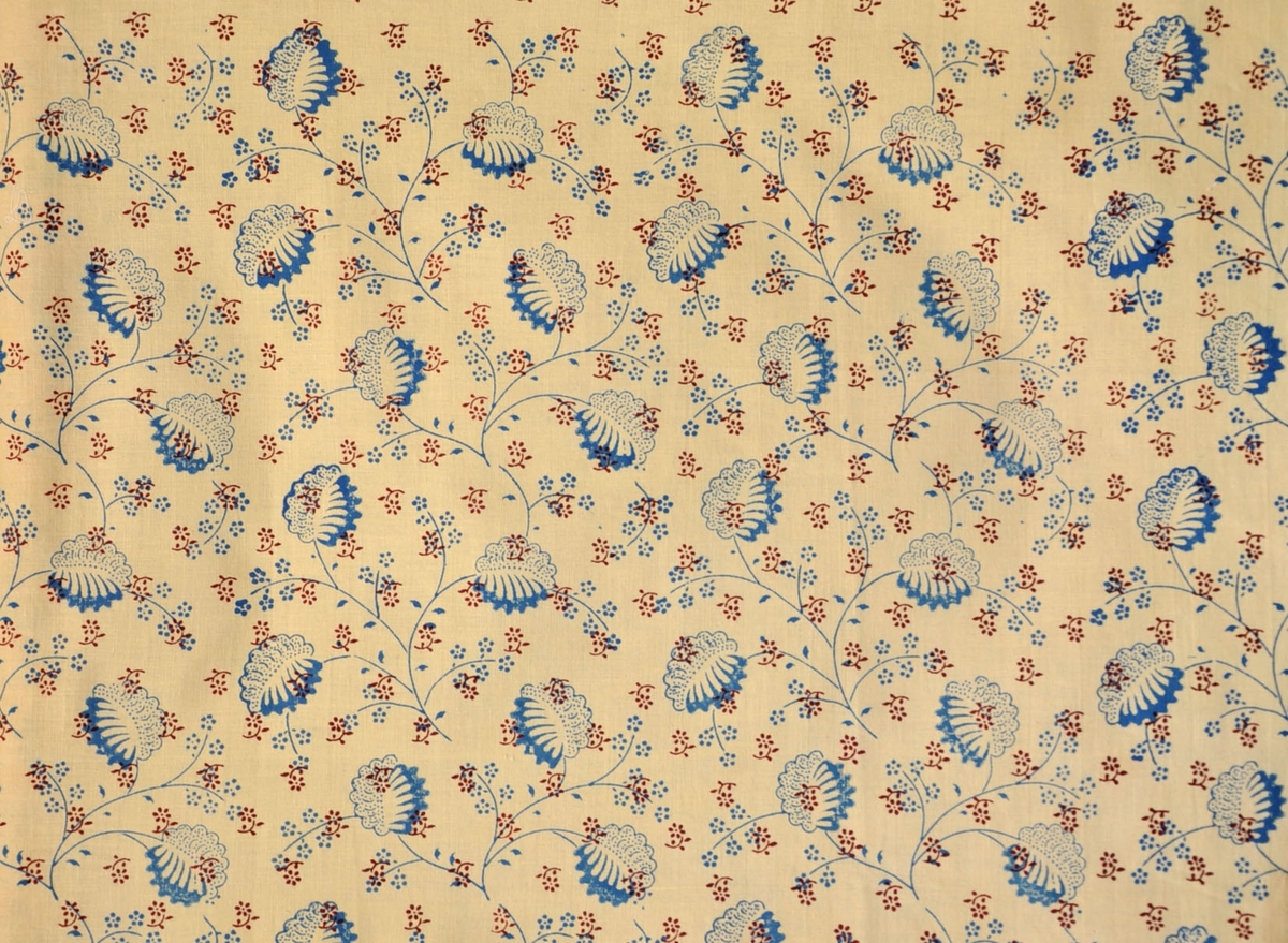 Bomullstyg, 1930-tal.
Klänningstyg med tryckt mönster med stiliserade blad och stjälkar med små blommor i rött och blått på styckfärgad bottenväv.
Rapport 17 x 34 cm
Antal tryckfärger 2
Valstryck
Pigmentfärg