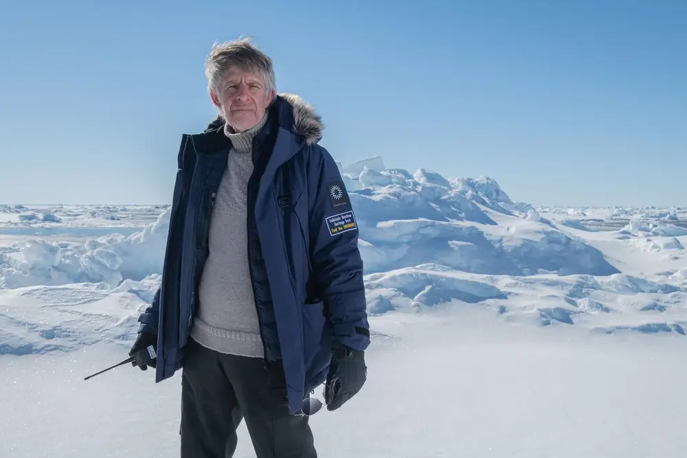 Bildet viser Mensun Bound med islagte omgivelser i bakgrunnen. Han har yttertøy på seg og en walkie talkie i den ene hånden. Det er sol og snø på bildet.