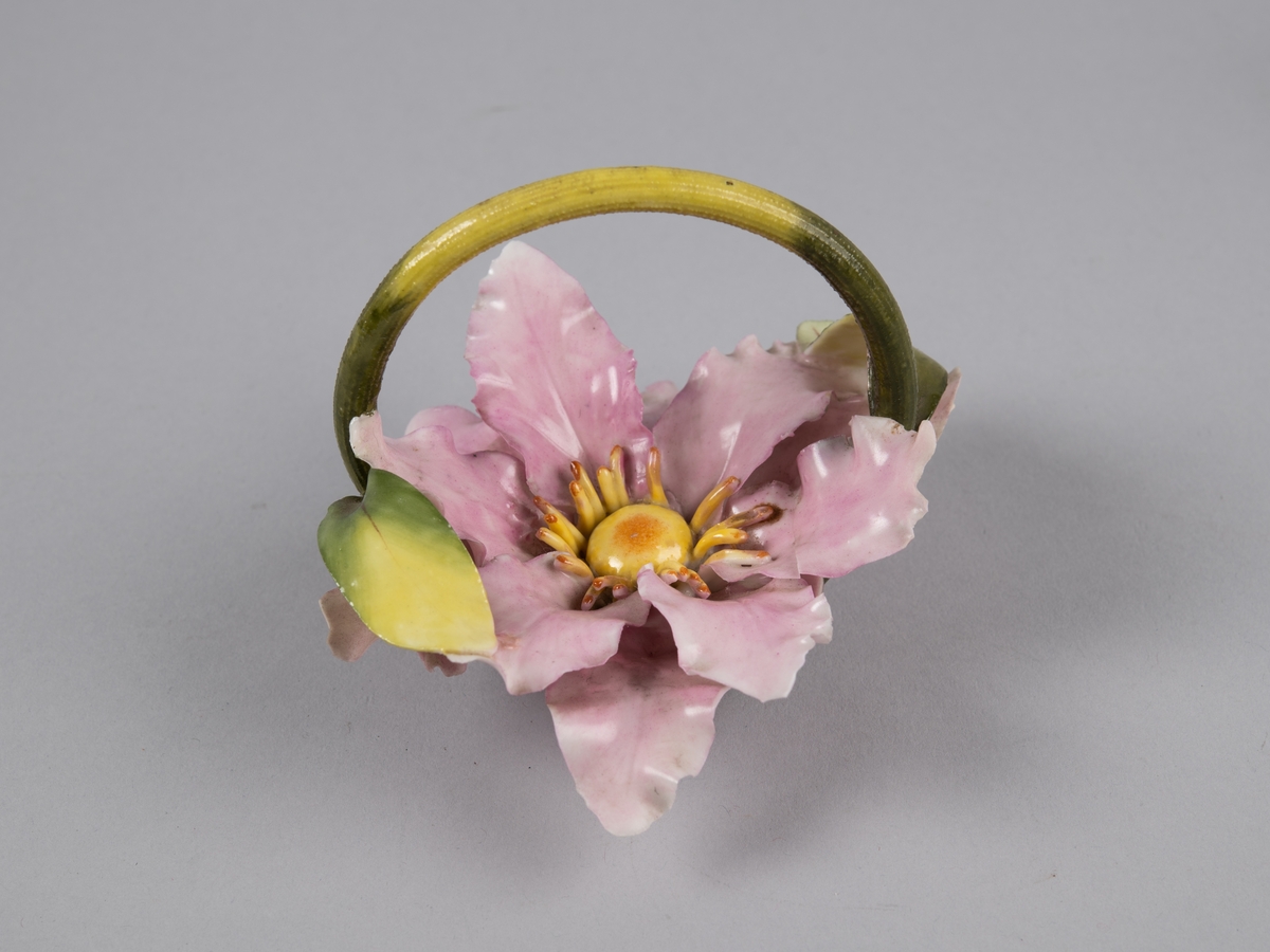 Modellert blomst med lange spisse kronblader. Formet som en kurv med hank over. Til borddekor.