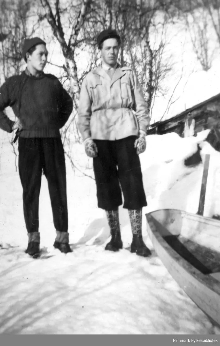 Einar Isaksen, og Rolf Sundquist utenfor gammen i Gokkmokka. Det er snø og de er kledt i skiklær. Til venstre ses en del av en båt, eller pulk