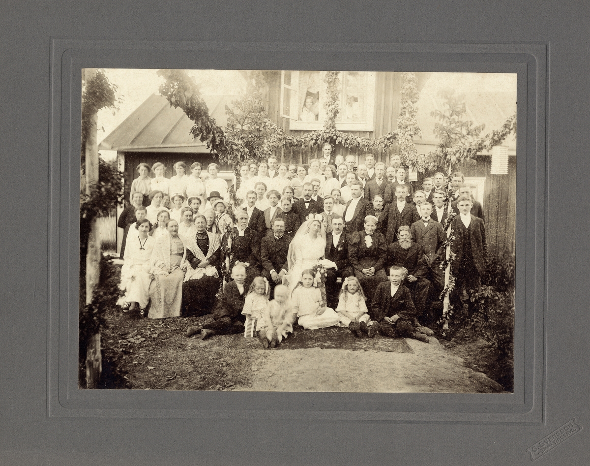 Ett bröllopsfölje med brudparet i mitten, utanför ett bostadshus i närheten av
Tingsryd, ca 1914.