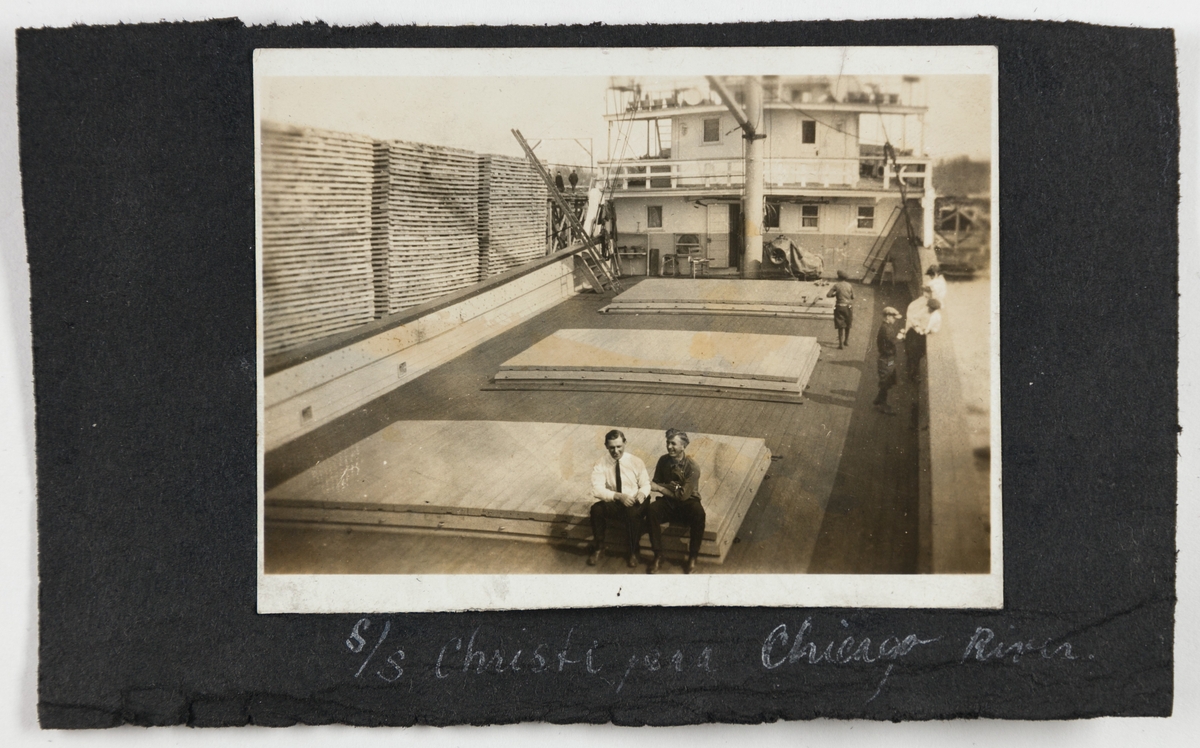 To menn og flere gutter på dekk på dampskipet D/S "Christie". En stor trelast står langs brygga til ved siden av skipet.