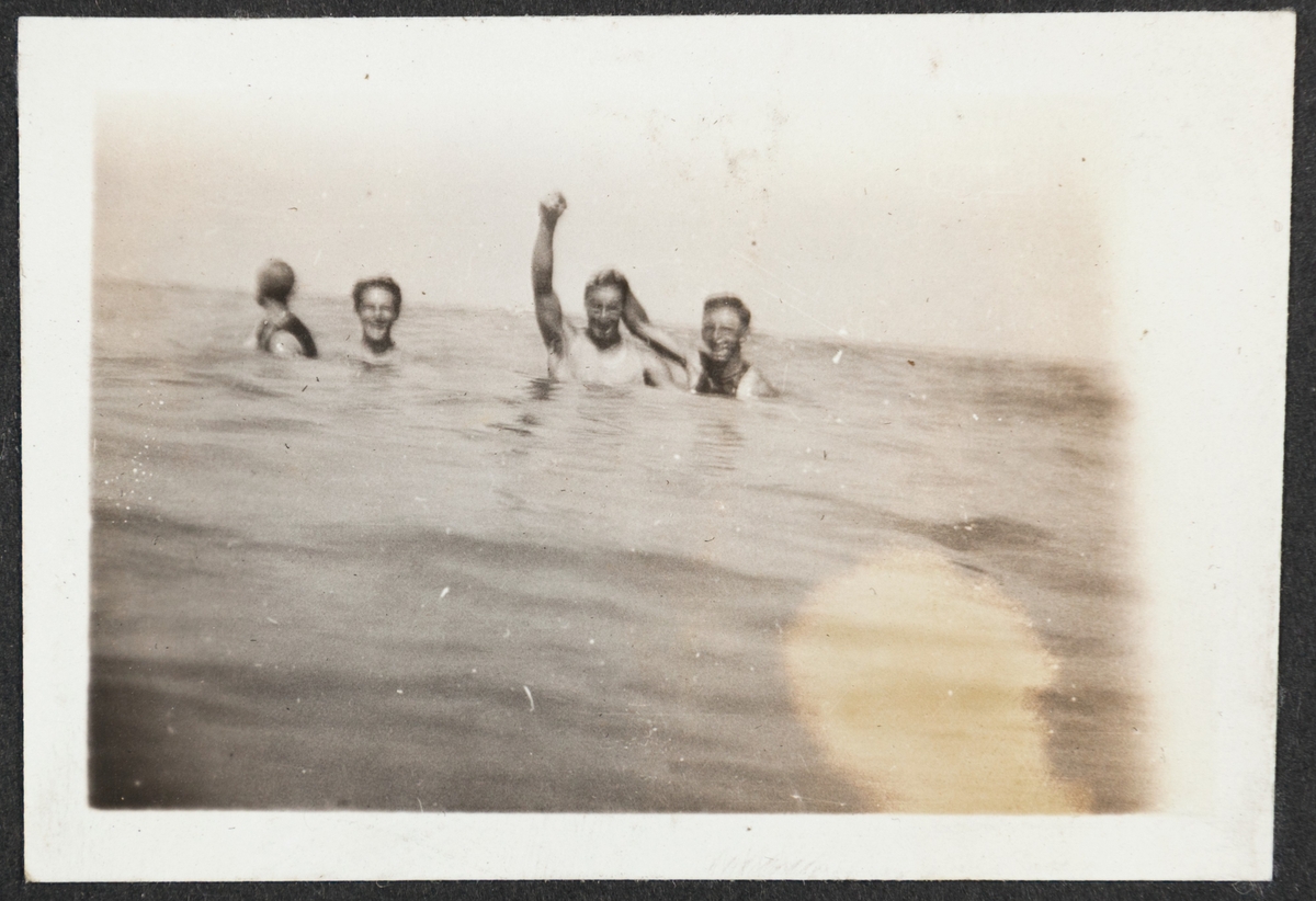 4 kamerater fotografert badende i sjøen. En av mennene løfter hånden i hilsen.