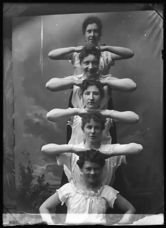 Five women in a human pyramid, stacked on top of each other with their elbows out so they make a sort of pattern