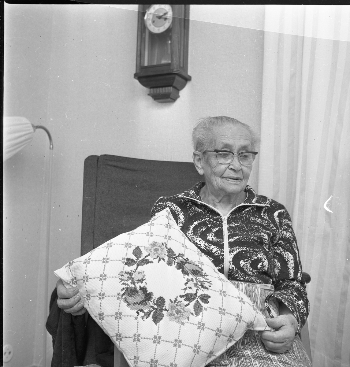 Äldre kvinna med broderad kudde.