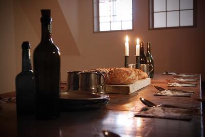 Nærbilde detaljer på et bord i folkestua i Eidsvollsbygningen. På bordet står ei flaske, et brød ligger på ei fjøl og i bakgrunnen ser vi to stearinlys