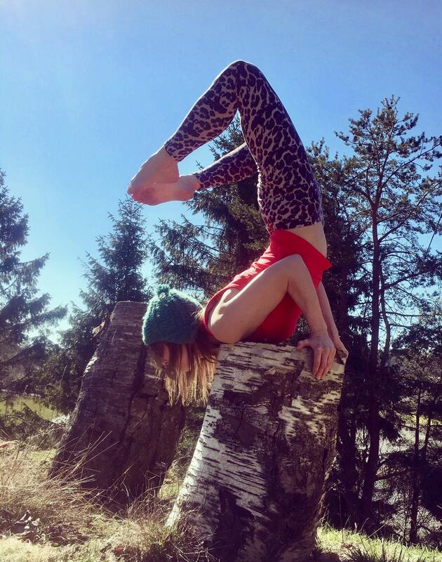 En kvinne gjør en avansert yogastilling på en stubbe i skogen.