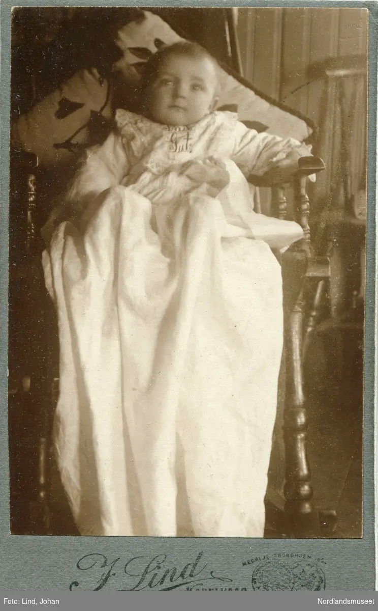Portrett av et spedbarn i dåpskjole, plassert på en gyngestol.