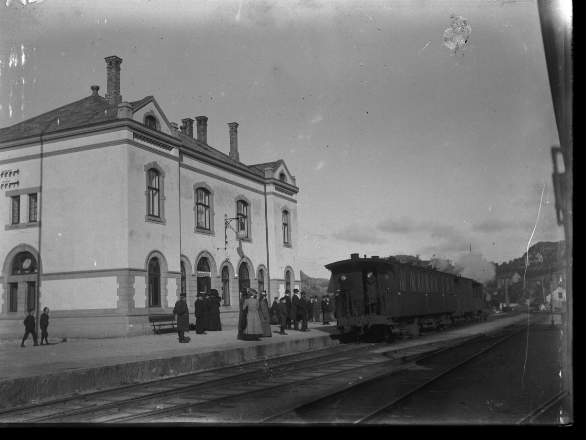 Egersund jernbanestasjon med et tog og mennesker på perrongen.
