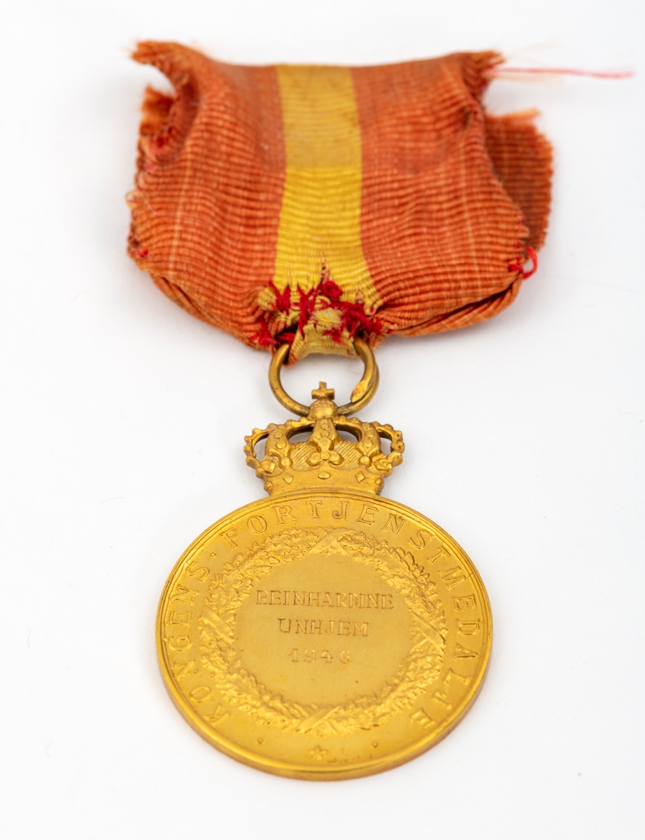Kongens fortjenstmedalje i gull, med bånd i rødt med gul stripe i midten; alt festet til ramme av tre. På forsiden av medaljen er et portrett av Kong Haakon, omkranset av teksten "Haakon VII Norges Konge. Alt for Norge."