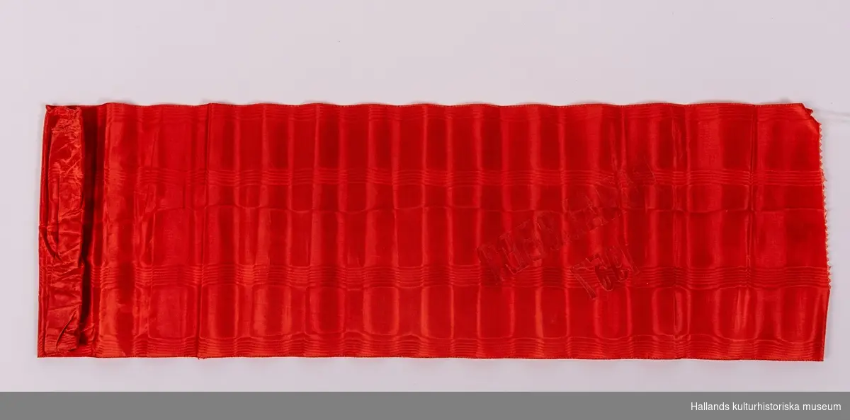 Rött konstsidenband med målad guldtext: "FONALÖBET 1957".