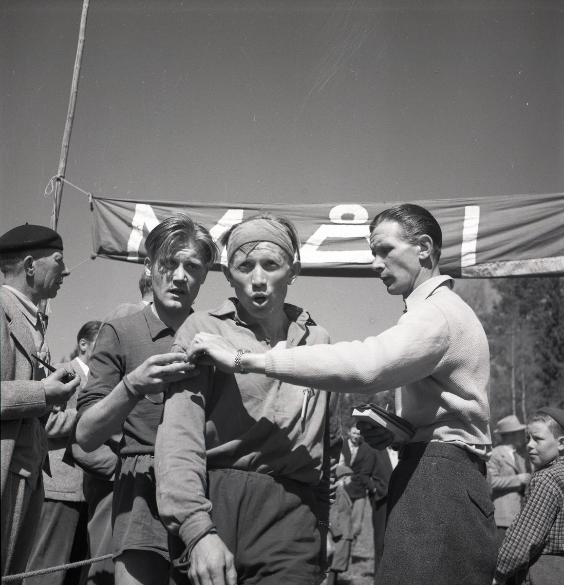 En orienterare går i mål under en tävling och tas om hand av funktionärer den 20 maj 1951 i Växbo.