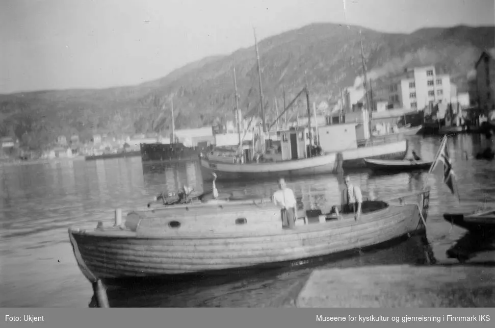 Bildet viser en motorbåt, også kalt for snekka, som legger til ved Nissenkaia i Hammerfest havn, trolig på 1950-tallet. I bakgrunnen ser man at Findus-fabrikken har kommet på plass allerede. På båten står det to menn som ser mot kameraet. I hekket av båten vaier det norskeflagget. I bakgrunn ser man Hammerfest kai og flere andre båter. Båten tilhørte mest sannsynlig familien Normann fra Melkøya.