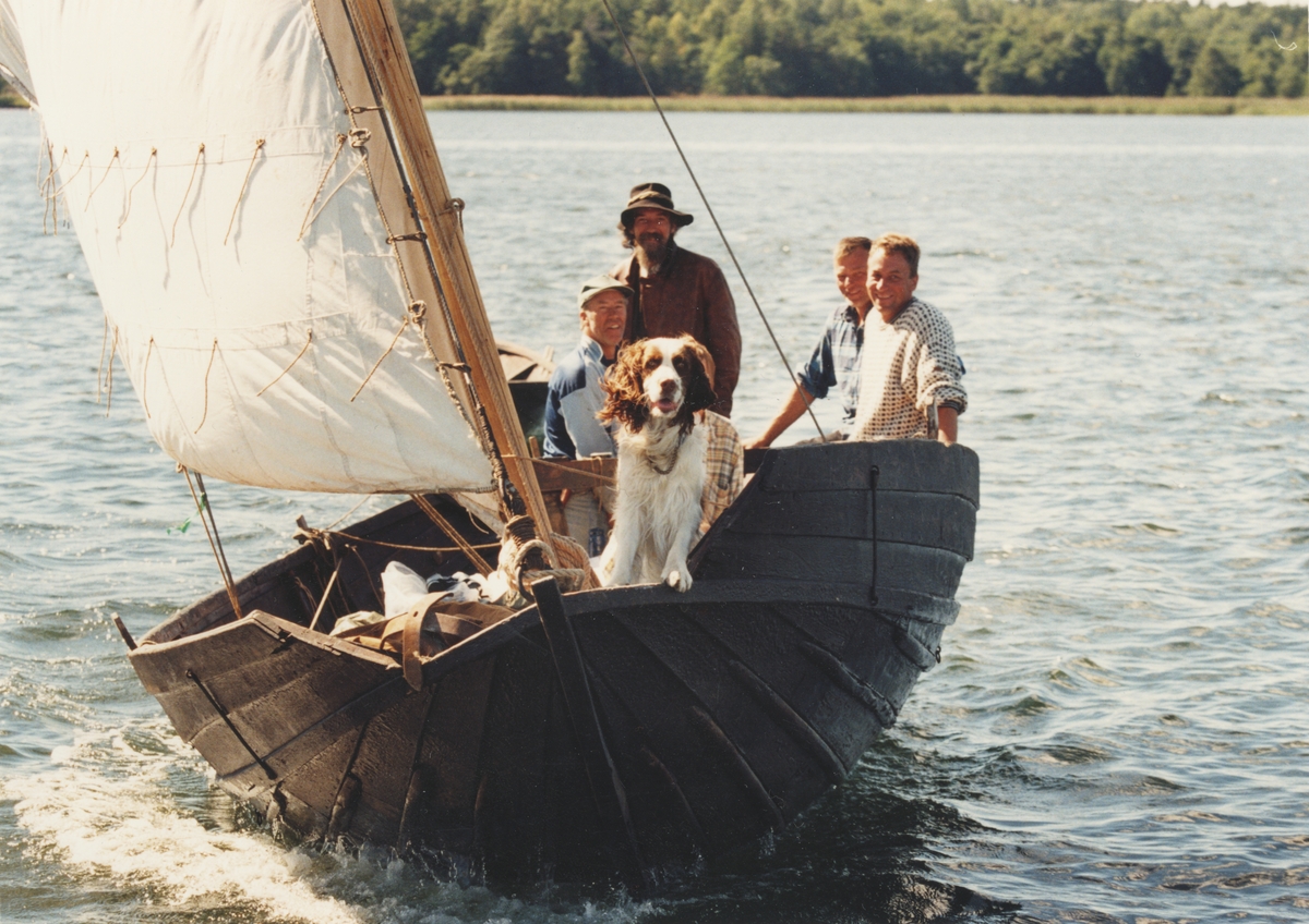 En levande museibåt seglar, fyra män och en hund samt en båt på släp, i samband med utställningen "Människor och båtar i Norden".