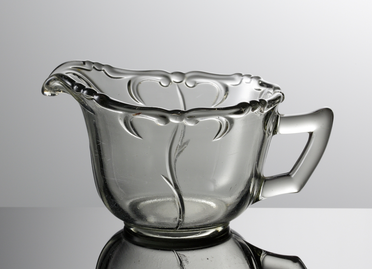 Pressad gräddkanna i rökfärgat glas. Motiv av stiliserade växter i relief.