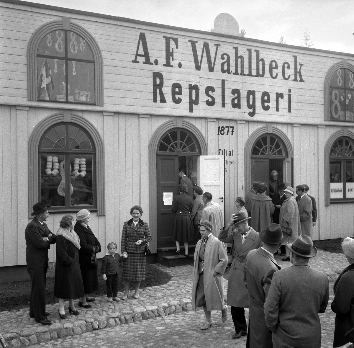Bildserie från invigningen av Wahlbecks repslagerimuseum i Gamla Linköping 1959. Kontorsbyggnaden uppfördes på 1860-talet av byggmästaren Jonas Jonson som hamnkontor och var placerad vid Linköpings hamn. Byggnaden inköptes 1877 av repslagaremästaren Adolf Fredrik Wahlbeck, som lät flytta den till firmans repslageri vid Kanberget där den nyttjades som kontor, butik och magasin. När Wahlbeck 1913 flyttade sin verksamhet till området söder om kyrkogården flyttades även denna byggnad för att 1944 inredas till museum. År 1957 flyttades såväl byggnaden som museet till Gamla Linköping. På bilderna ses bland andra bröderna Gotthard och Ebbe Wahlbeck och den förstnämndes son Olle Wahlbeck.