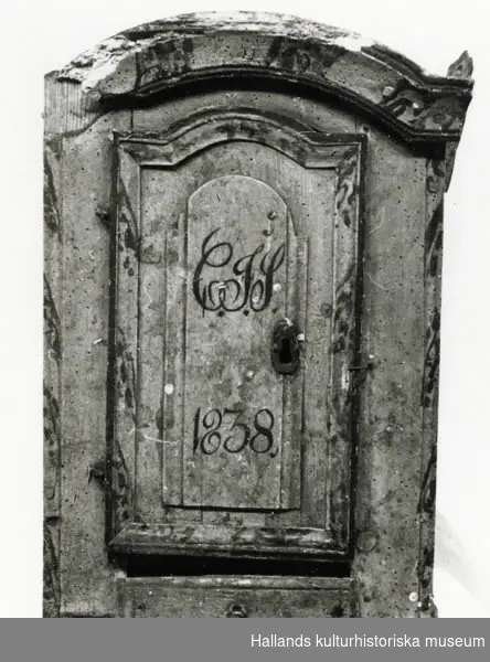 Skåp med en dörr. Inuti skåpet en hylla och nedanför dörren en låda. Skåpet är målat i blågrönt med marmorerade kanter. På skåpsdörren ett monogram "CIS 1838."