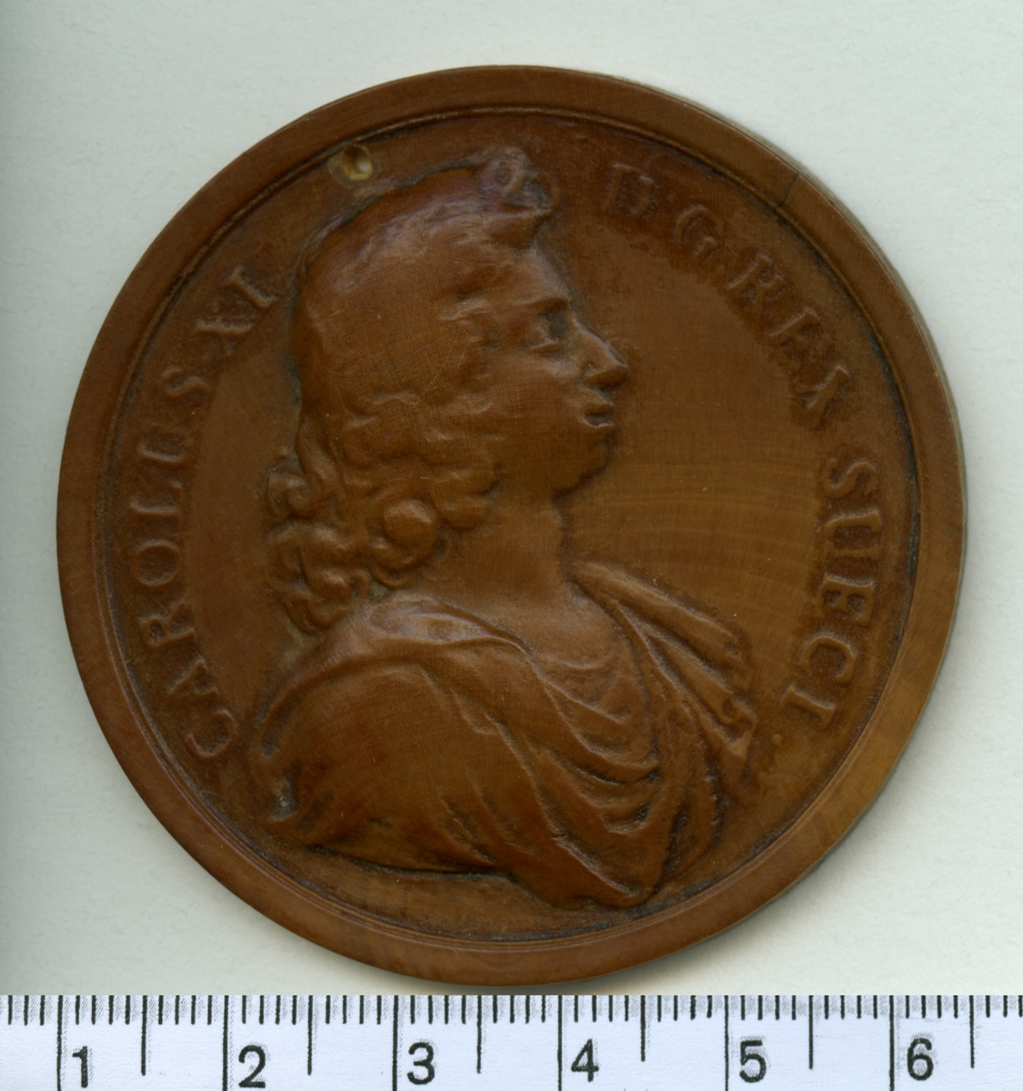 Modell till minnespeng i trä, visande Karl XI:s bröstbild.

Åtsida inskription: CAROLUS XI D G REX SUECI

Frånsida inskription: -