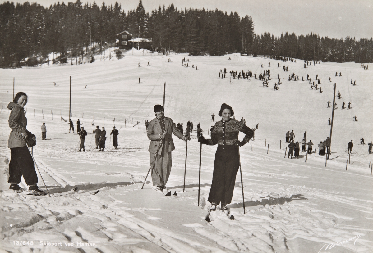 Postkort, Furnes, folk går på ski på jordene til Østre Alu gård, Gubbestua i bakgrunnen, skiantrekk, Gubbestua ble innviet 4. september 1910 tegnet av A. Halvorsen,