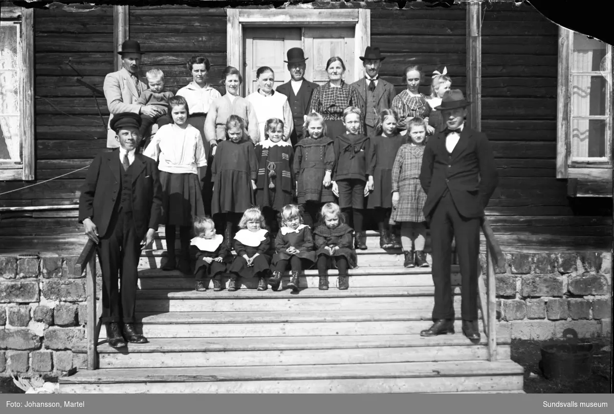 Gruppbild på trappen till Nybruket, arbetarbostäder vid Sörfors bruk. En stor grupp med vuxna och barn som bodde i huset.