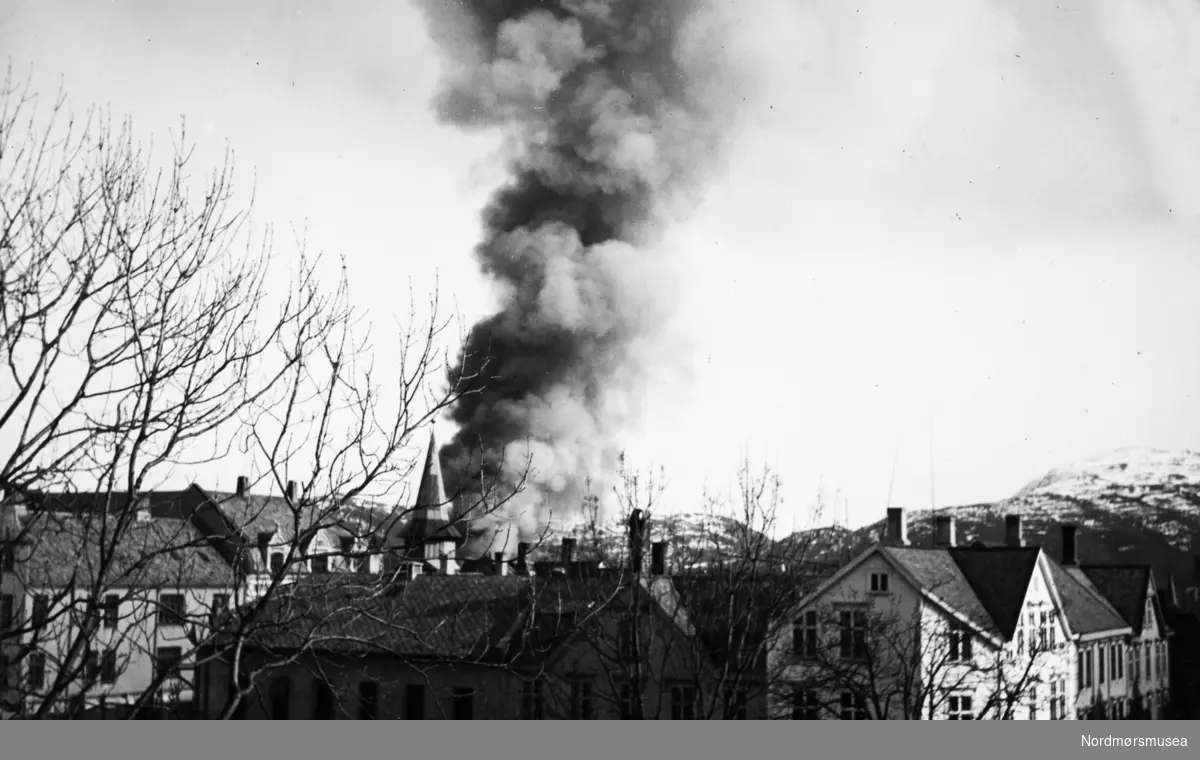 Kirkelandet i Kristiansund brenner og dagen er 28. april 1940. Her ser vi røykskyen stige opp over byen tidlig denne søndags morgenen. Bildet er tatt fra Georg Sverdrups privatbolig i Rosentræders gate 1.