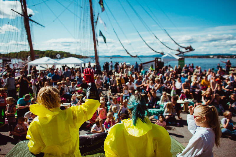 Aktivitører i gule drakter viser frem funn fra havet foran en stor folkemengde