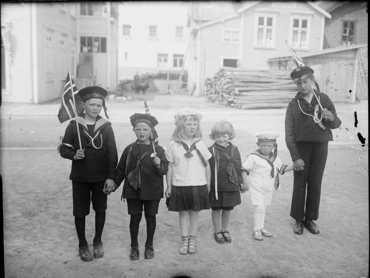 Barn i matrosdresser og matroskjoler med flagg, 17. mai. Bildet er tatt en gang mellom 1930 og 1940.  I bakgrunnen ser man Gamle Elvarheim / Borgengata.