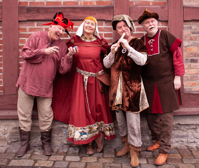 tre menn og en dame kledd i røde og hvite middelalderdrakter. En av dem spiller blokkfløyte