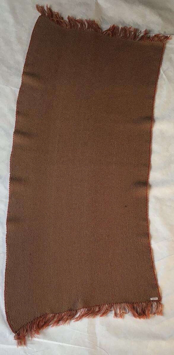 Stolteppe i vevd ull. Den er orange og brun med buet form.