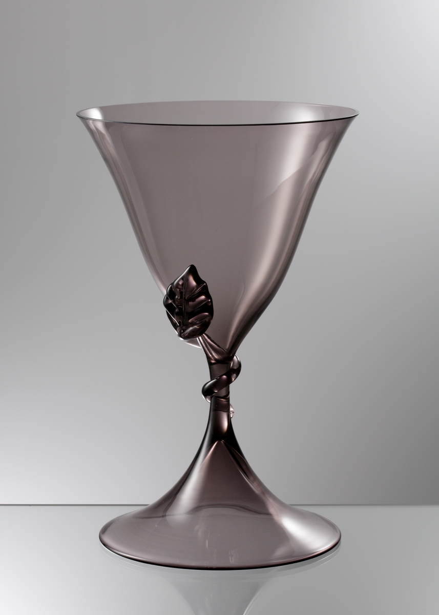 Brun vas formgiven av Simon Gate, tillverkad på Sandviks glasbruk. Fot och kupa blåsta. Påklippt och format löv på skålens nedre del.