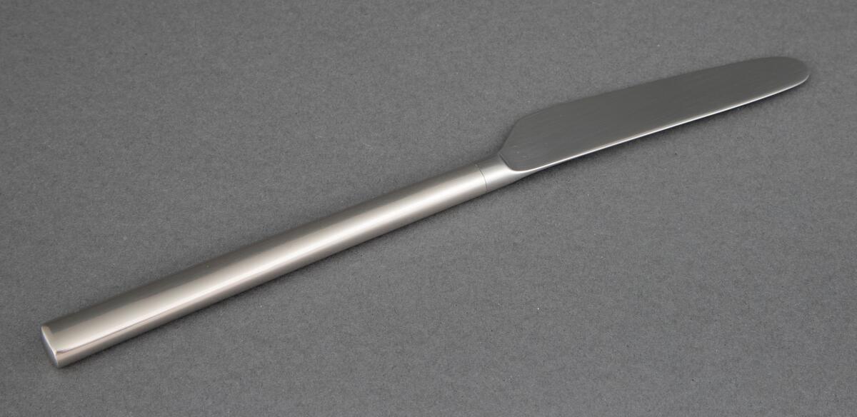 Bordkniv i presset rustfritt stål med rett linje fra bladrygg til skaft, smalt knivblad med små tagger og smalt skaft som tiltar noe i bredde og har rett avslutning.