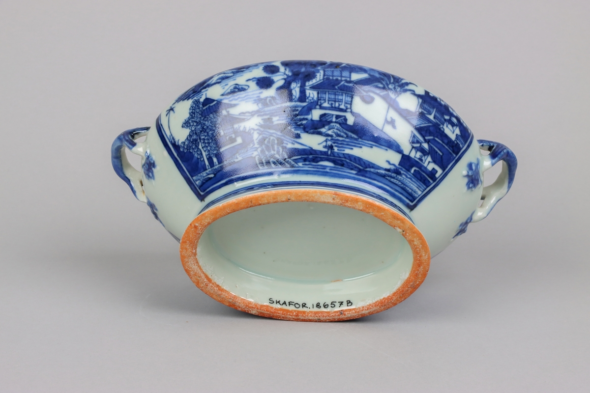Oval, lobed bowl with angular handles, supported on a central foot. On the both sides decor of landscape scenes of pagodas, buildings, gardens and waters. Handles in shapes of bent tree branches. On the foot a  dark blue border with rectangular reserves filled with symbols of fortunes. All decor in blue underglaze. The base of the bowl  with unglazed ring.