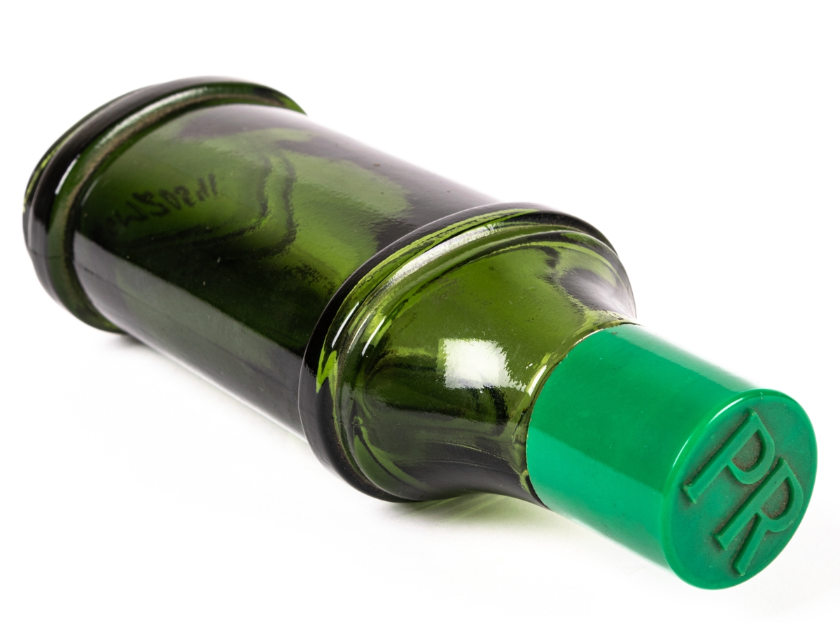 Flaska av brun-grönt glas med skruvlock i grön plast. Flaskan är ovalt rundad med bredare fram och baksida längst ned. Vid ca 2/3 höjd av flaskan finns en utstående list i glaset runt hela flaskan. Över den övre listen avsmalnar flaskan uppåt. Flaskan avsmalnar något nedåt mellan listerna. På framsidan under övre listen går en utbuktning i glaset. Under den står i vitt texten "PR ORIGINAL PR FOR MEN PIERRE ROBERT HAIR LOTION DRY". På locket i utstående bokstäver står det "PR". Fabrikationstryck i glaset i botten: "KG".